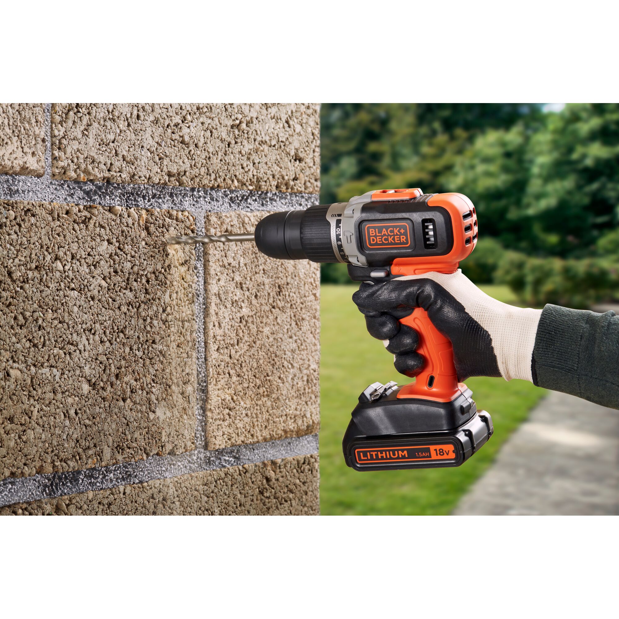 A person wearing gloves uses a BLACK+DECKER cordless drill to drill into a concrete block wall outdoors. The drill is orange and black and labeled with 'BLACK+DECKER' and 'LITHIUM 18V.'