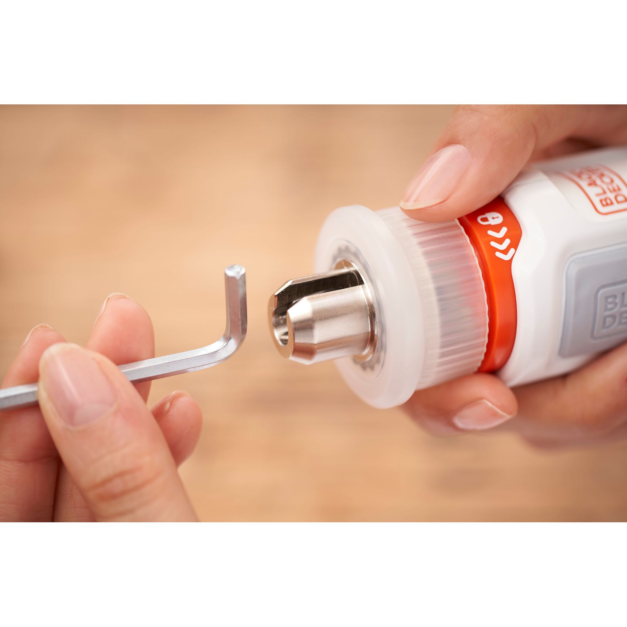 Close-up of a person's hands holding a BLACK+DECKER tool with a metal chuck, using an L-shaped hex key for adjustment or installation.