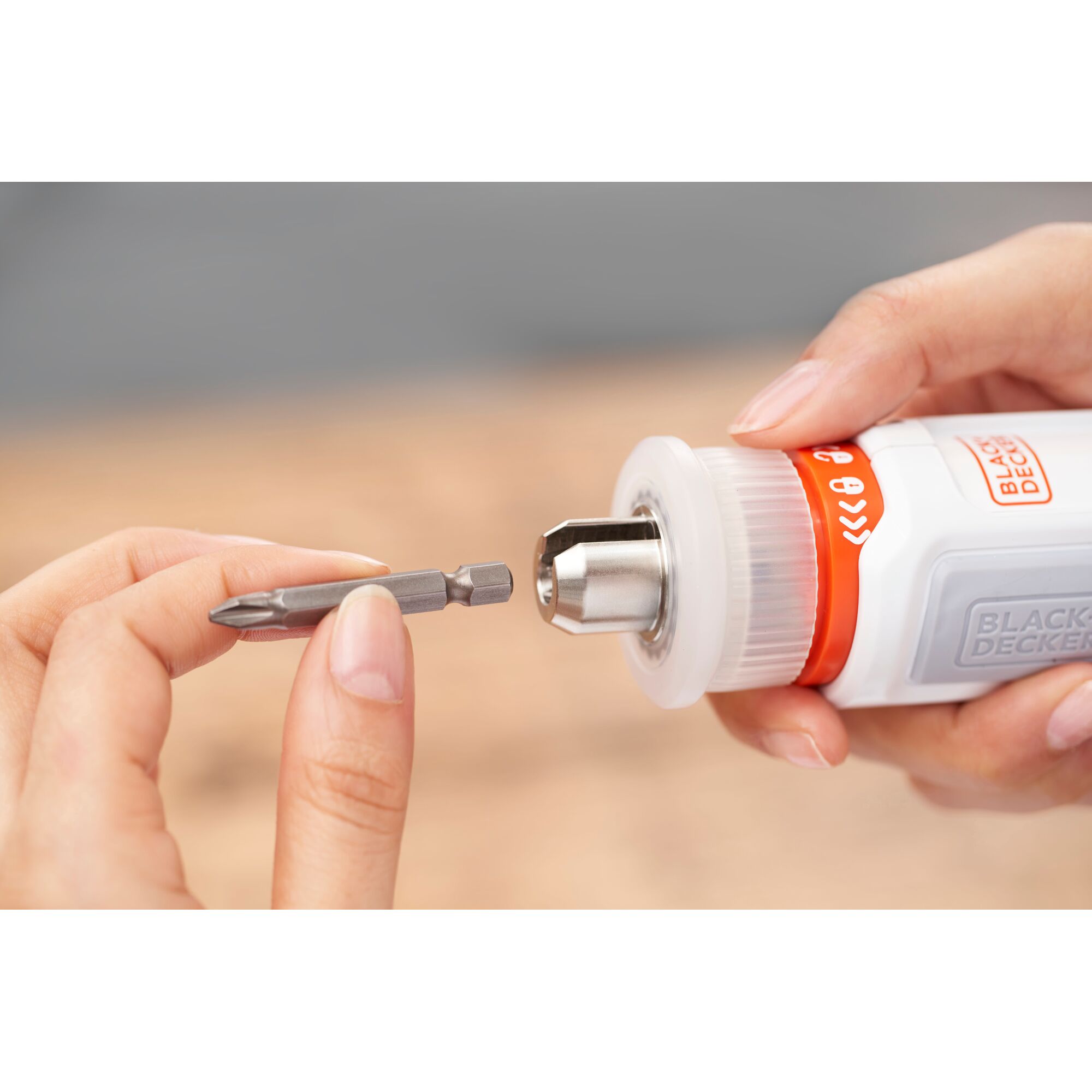 Close-up of hands holding a BLACK+DECKER tool, with one hand inserting a screwdriver bit into the tool's chuck.
