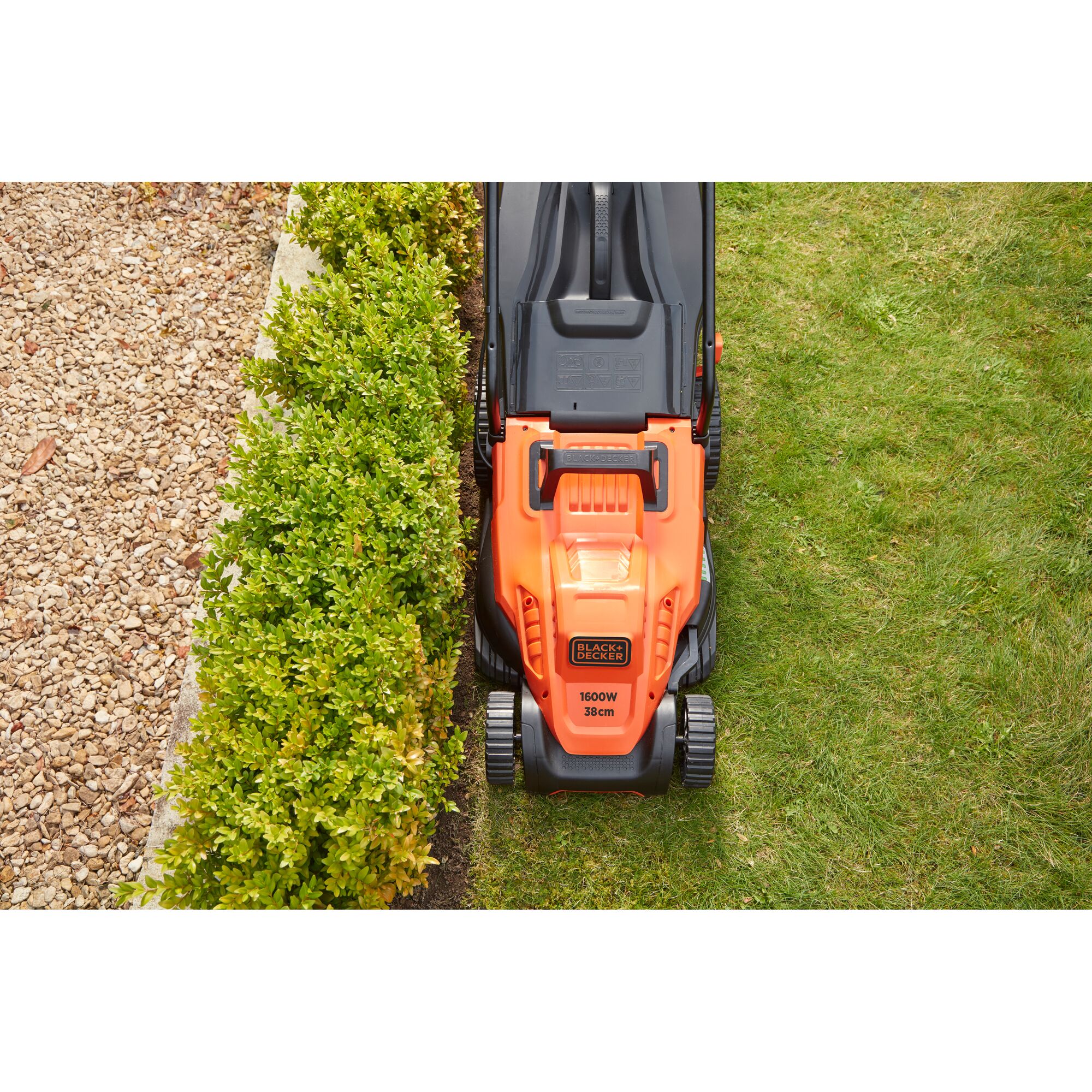 Photo of BLACKDECKER BEMW471BH orange lawn mower cutting grass next to green hedge and gravel path.
