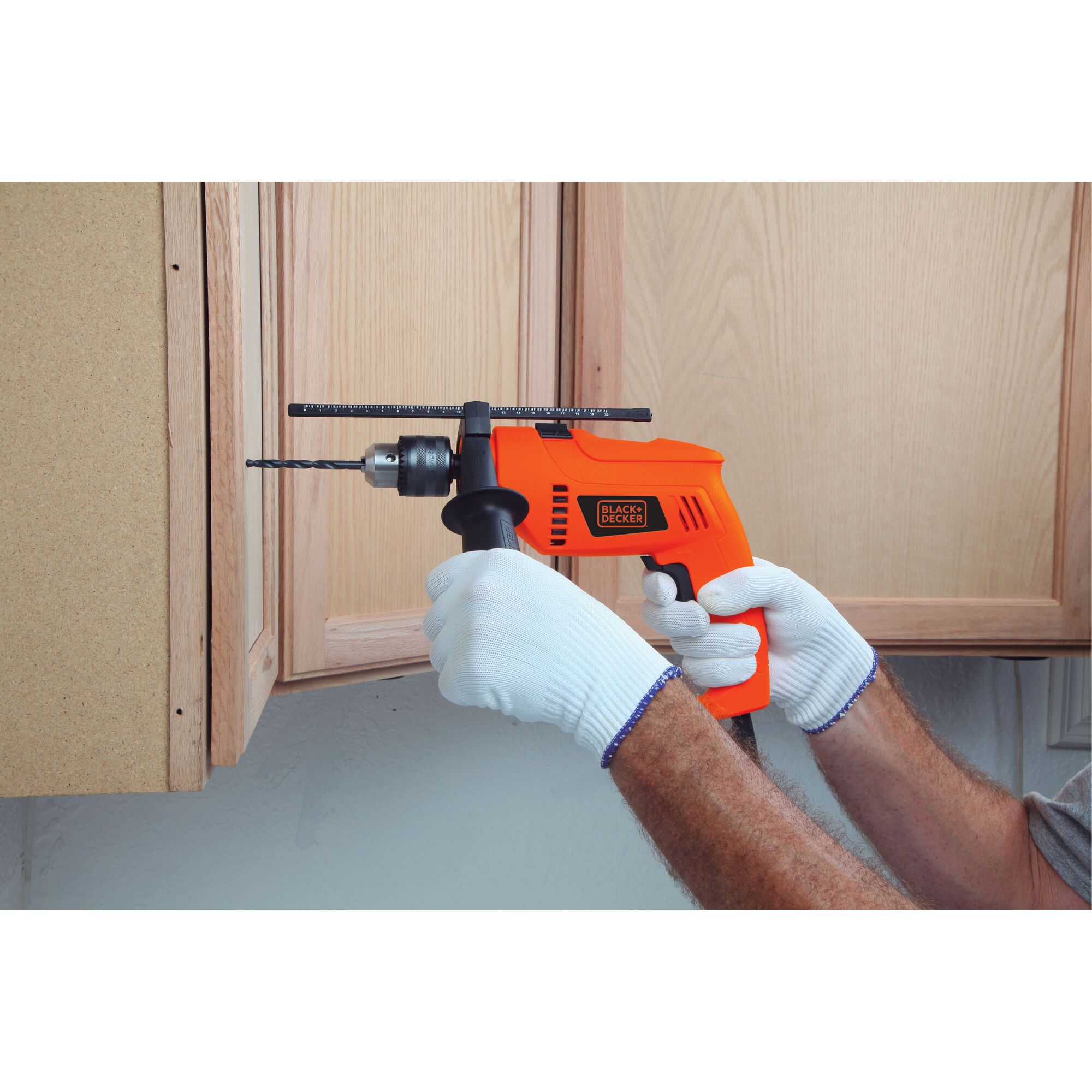 BLACKDECKER HD555 orange corded drill in use, drilling into wooden cabinet, user wearing white gloves.