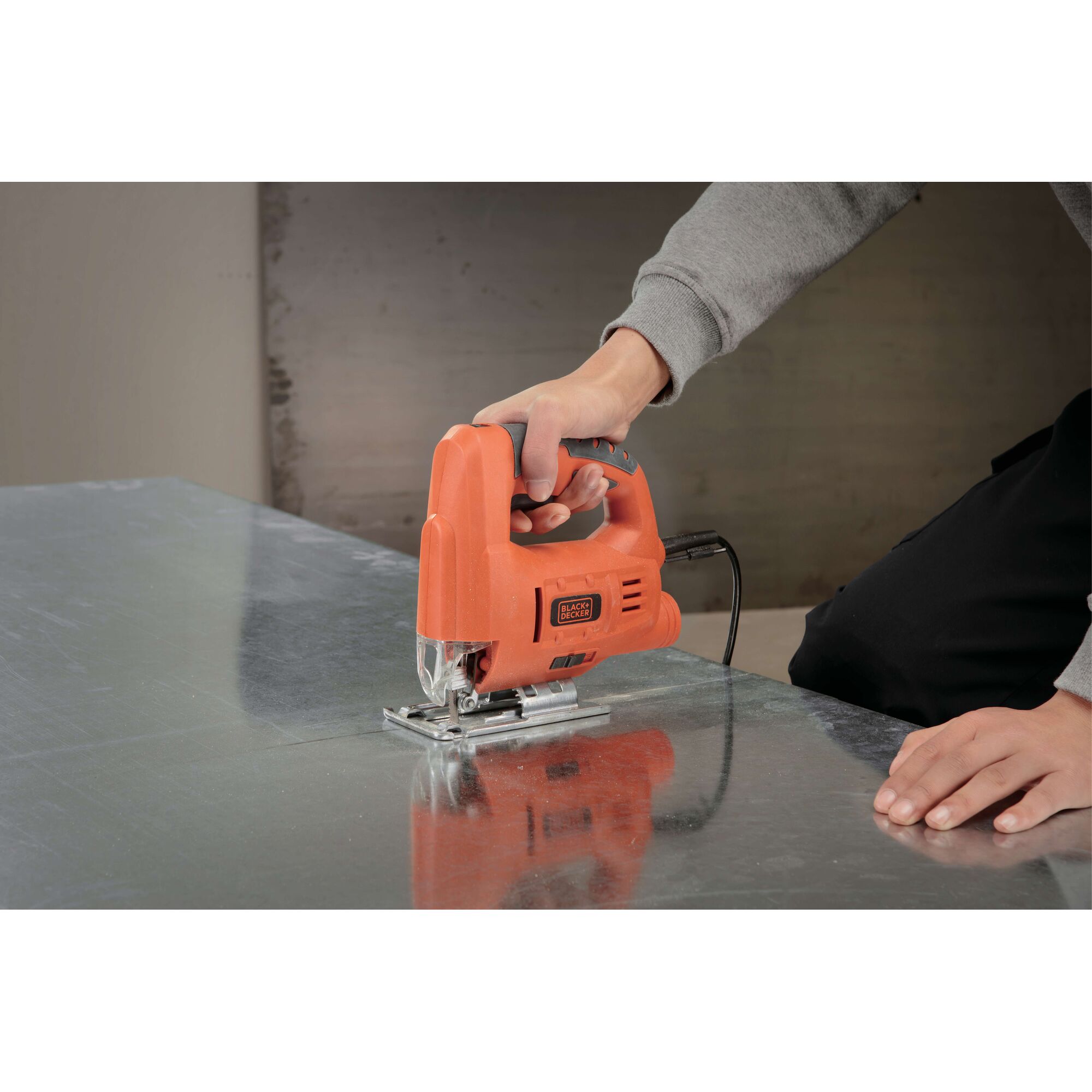 BLACKDECKER JS20 jigsaw in use cutting metal sheet, orange body, photography of product in action.