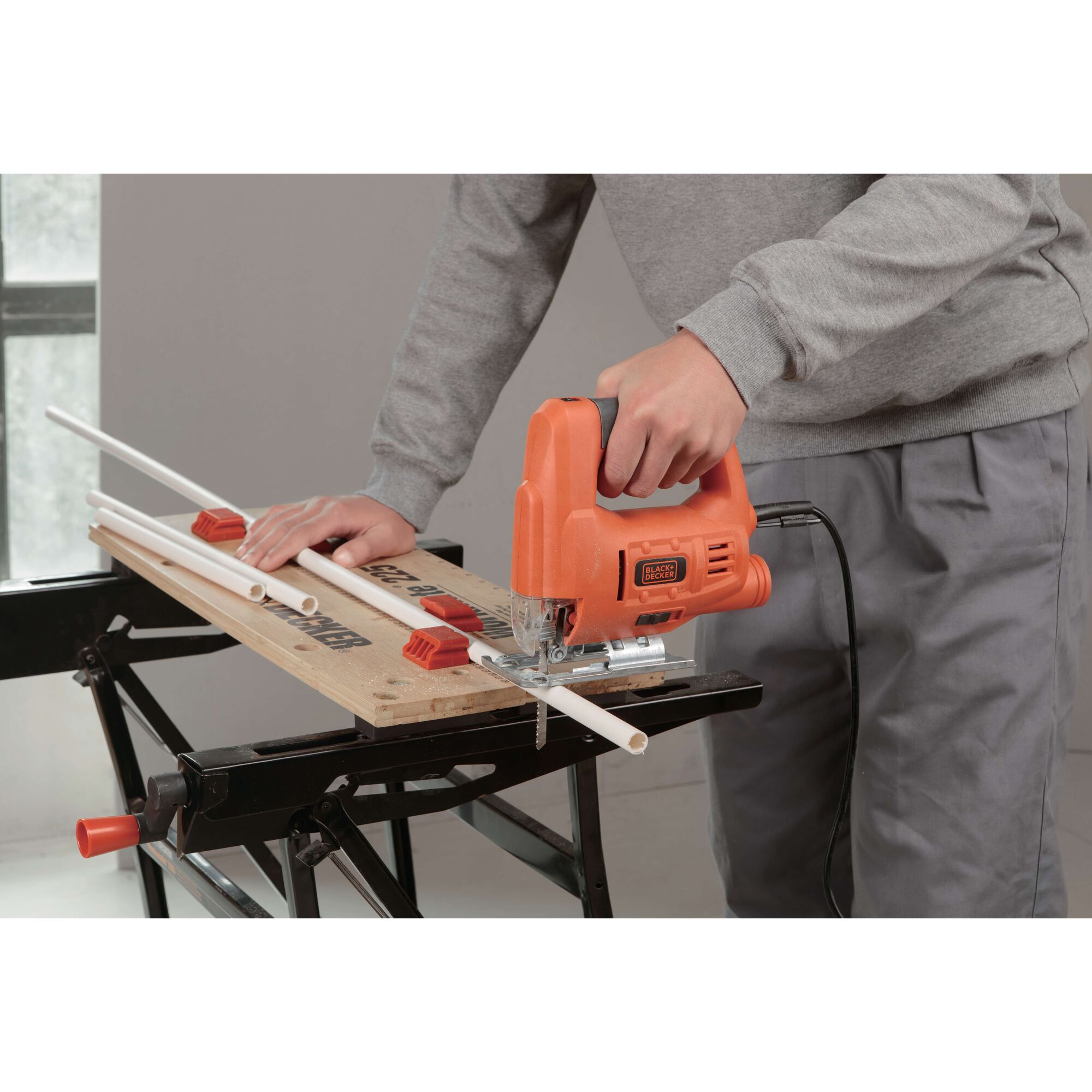 BLACKDECKER JS20 jigsaw used to cut a white pipe on a workbench, close-up view.