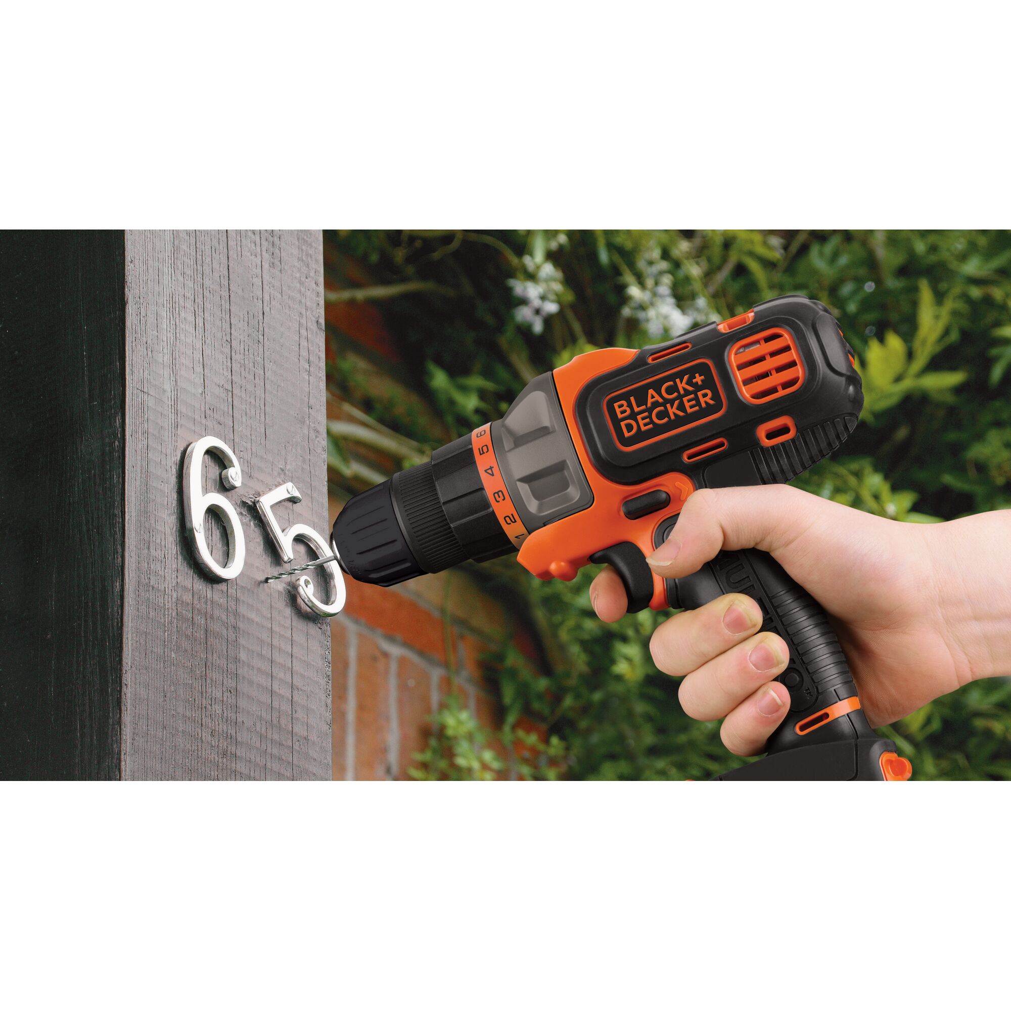 BLACK+DECKER MT218K cordless drill in use, drilling metal numbers into outdoor wood post.