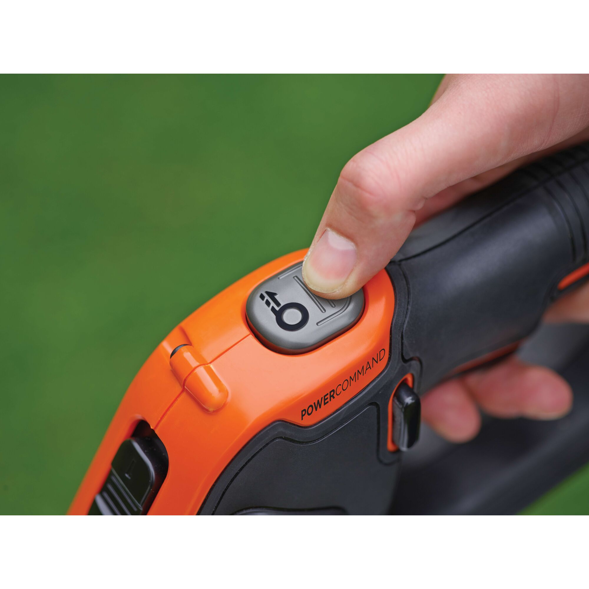 Close-up of a hand pressing the Powercommand button on an orange and black BLACK+DECKER device, with a green background.