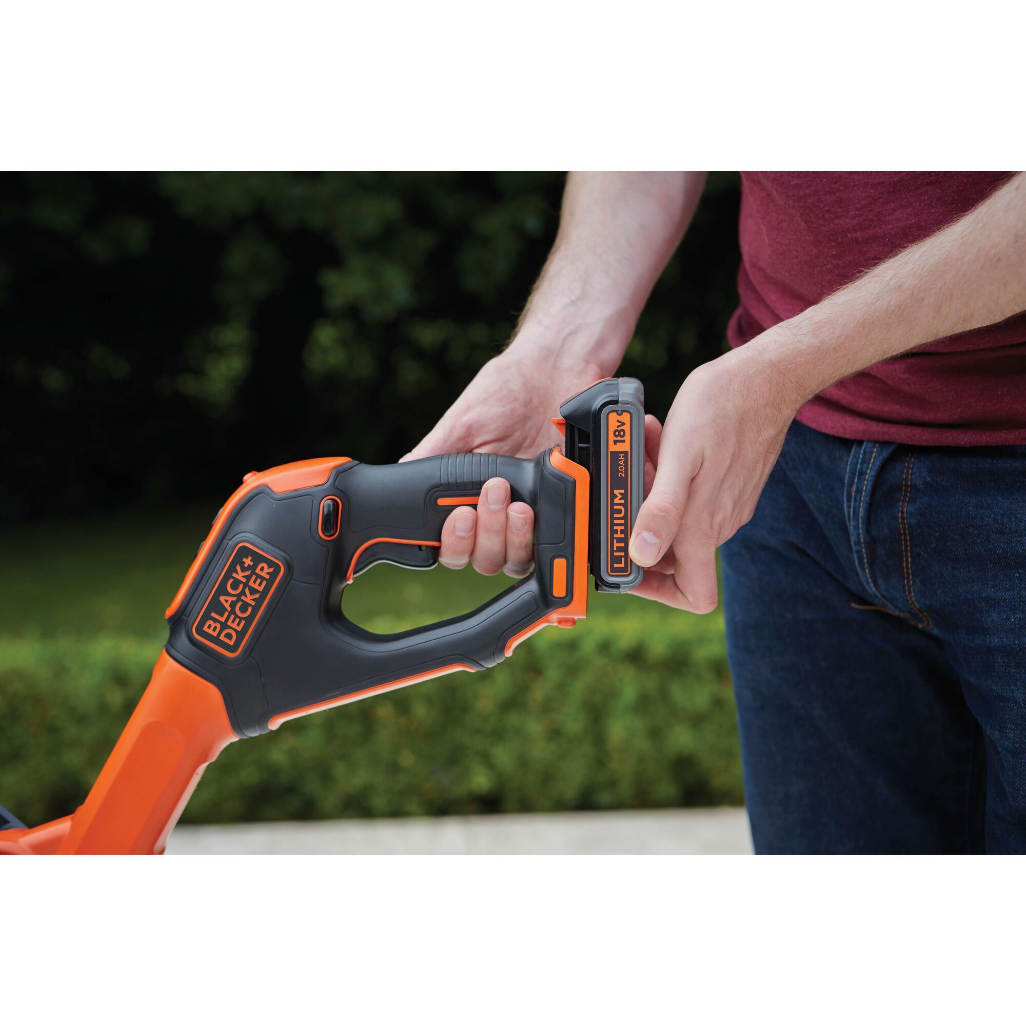 A person is inserting an 18V lithium battery into a BLACK+DECKER cordless power tool outdoors.